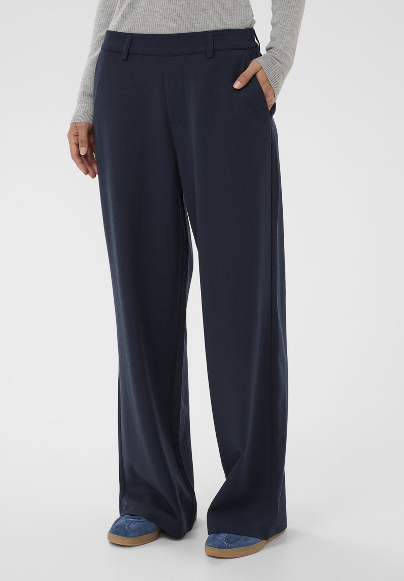 Navy wide-leg trousers with a smooth texture, featuring a fitted waistband and side pockets, styled with blue suede shoes.