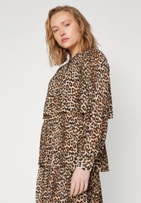 Blusa a strati con stampa leopardata in tonalità di marrone, con maniche lunghe, polsini a bottone e un design ampio e fluido. Tessuto texturizzato.