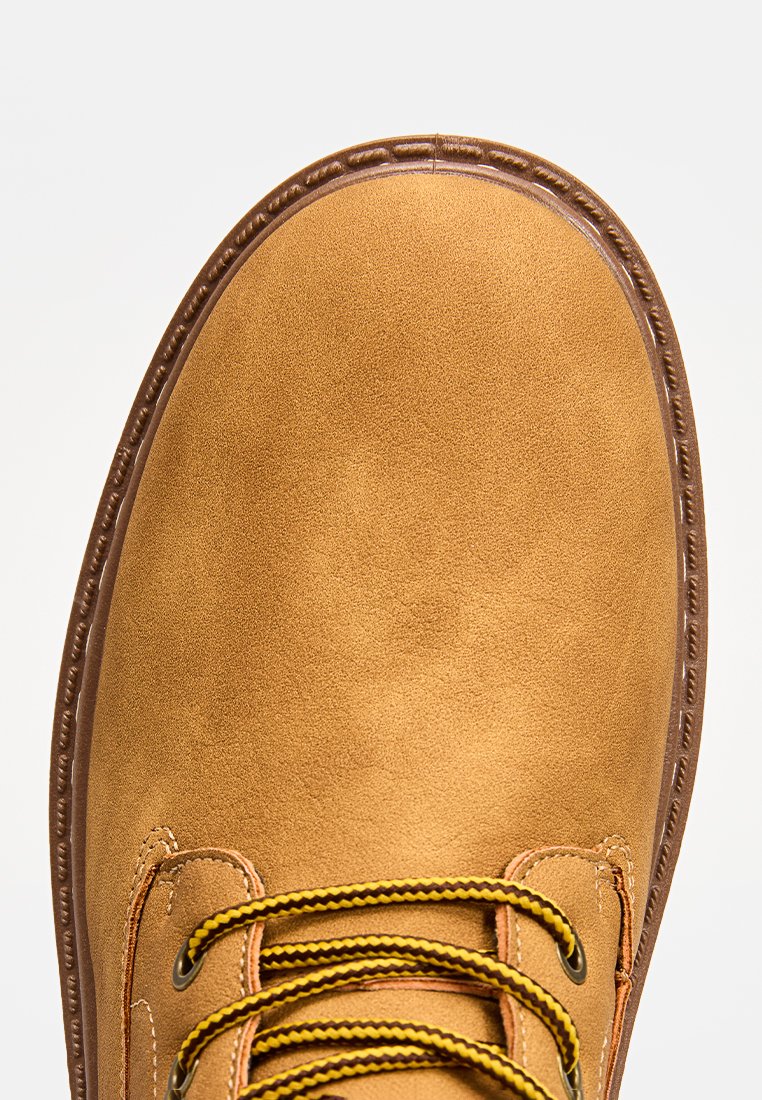 Stivale in pelle scamosciata marrone con punta tonda, lacci gialli e neri, e suola marrone in contrasto. Parte superiore texture e dettagli di cucitura visibili.