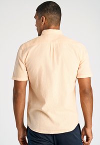 Korte mouwen overhemd in licht perziktweefsel, met een rugpand en plooi detail, met een gladde textuur en een iets gebogen zoom.