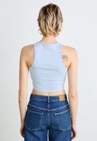 Light blue cropped tank top made from a soft, stretchy material. Worn with high-waisted blue jeans featuring back pockets.