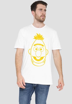 Weißes Baumwoll-T-Shirt mit einem großen gelben Druckmotiv eines Cartoon-Charakters, das aus einfachen Formen und minimalen Details besteht.