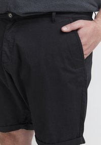 Shorts de algodón negro con una textura suave, que presentan bolsillos laterales, un dobladillo enrollado y un cierre de botón en la cintura. Diseño simple.