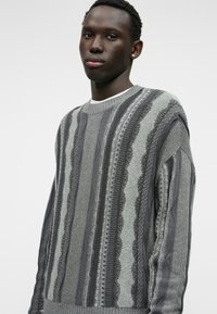 Γκρίζος πλεκτός σινίωτας με μοτίβο εναλλασσόμενων οριζόντιων κυμάτων, που διαθέτει υφή ρίγες και σχέδιο με στρογγυλή λαιμόκοψη.