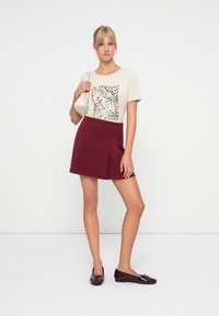 Crème t-shirt met een luipaardprint, gecombineerd met een bordeauxrode geplooide rok en donkere glanzende ballerina's. Inclusief minimalistische handtas.