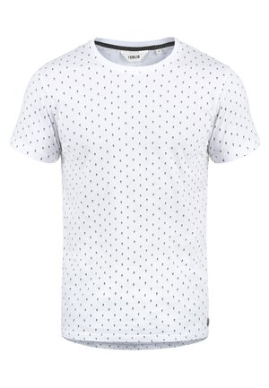 White short-sleeve t-shirt with black polka dot pattern and round neckline. Soft cotton fabric with a straight cut and a tag at the hem.