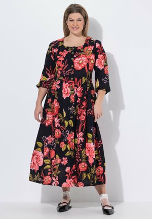 Kvinde iført en sort knap-op midi-kjole med store pink og røde blomsterprints, kombineret med gennemsigtige hvide sokker og sorte ballerinaer.