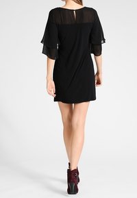 Musta mekko, jossa on läpikuultavat kerrokselliset hihat, avaimenreikäselkäyksitys ja rento malli. Yhdistetty burgundinvärisiin mokkasiiniin.