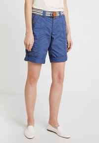 Pantaloncini di cotone blu con orli arrotolati, dotati di più tasche, chiusura con bottoni e cintura a righe con fibbia marrone.