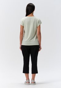 Top de color verde claro de manga corta y corte holgado, combinado con pantalones cortos negros. La tela parece suave y tiene una textura lisa.