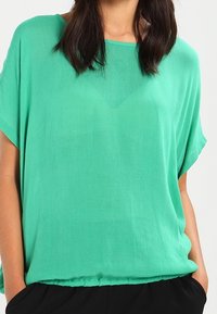 Blusa verde a maniche corte realizzata in tessuto leggero, con orlo inferiore elasticizzato e una vestibilità morbida.