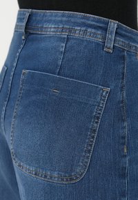 Jeans de denim em lavagem média com cintura alta, com um bolso traseiro, costura em contraste e uma textura suave.