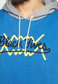 Felpa blu con cappuccio grigio, caratterizzata da scritte nere ricamate "Black Fives" e dettagli gialli a zigzag. Laccetti bianchi regolabili.