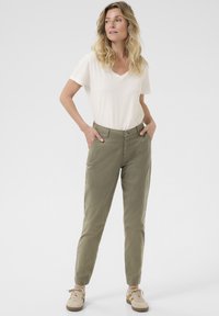 Chino kaki con vestibilità slim, dotati di chiusura a bottone, tasche laterali e polsini elastici. Abbinati a una t-shirt bianca a scollo a V.