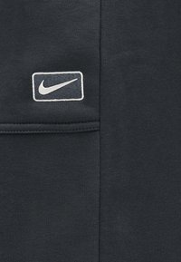 Σκούρο ύφασμα με ένα ραμμένο ορθογώνιο έμπλαστρο που φέρει το λευκό λογότυπο Nike swoosh σε μαύρο φόντο.