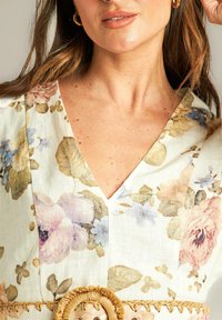 Vestido de estampado floral en tejido ligero, con escote en V y un cinturón trenzado con un acento circular. Los colores incluyen tonos pastel y beige.
