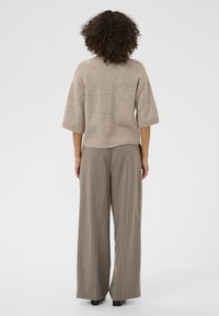 Beige strikket sweater med korte ærmer, ribbet kant, kombineret med lysebrune, vidde bukser med hårlinje-striber. Set bagfra mod en ensfarvet baggrund.