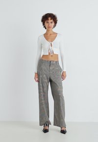 Hvit cropped topp med knyting foran, sammen med mønstrede vide bukser med flerfargede striper. Svarte spisse tøfler.