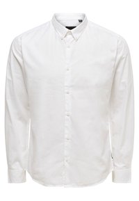 Chemise blanche à manches longues et boutons, fabriquée en coton, avec un col classique, des boutons à l'avant et des poignets ajustés avec des détails de couture visibles.