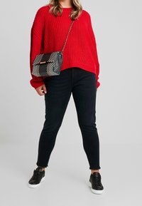 Czerwona sweter z dzianiny z długimi rękawami, zestawiony z czarnymi dopasowanymi dżinsami i czarnymi sneakersami. Torba ma wzór w kratkę, łańcuchowy pasek i zapięcie klapowe.