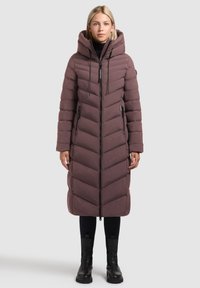 Lang, hættepufferjakke i dyb mauve med et chevron-quiltet mønster, lynlås lukning foran og sidelommer. Sammen med sorte leggings og støvler.
