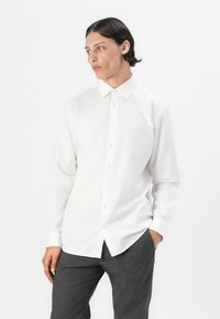 White long-sleeve shirt with a spread collar, front buttons, and a smooth cotton texture, paired with gray trousers.