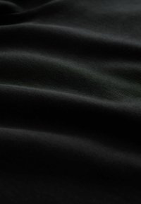 Tela negra con una textura suave, que presenta sutiles ondas y pliegues, reflejando poca luz y creando una apariencia suave y matizada.