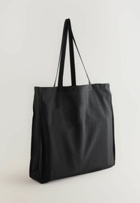 Black canvas tote bag with long shoulder straps, rectangular shape, smooth texture, and no visible patterns or hardware details.
