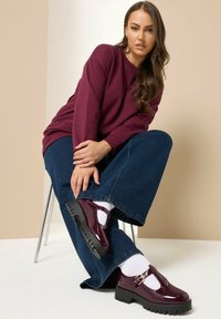 Zapatos de plataforma de charol burdeos con suela gruesa y recortes laterales, combinados con calcetines blancos y denim, llevados con una camisa de manga larga.