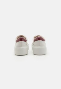 Baskets plateforme blanches avec une finition en cuir lisse, présentant un accent bordeaux brillant au niveau du talon et une doublure en tissu texturé.