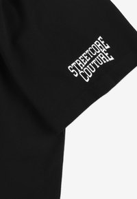 Czarny t-shirt z krótkim rękawem z białym nadrukiem "STREETCORE COUTURE" na rękawie. Gładka bawełniana tkanina, regularny krój.