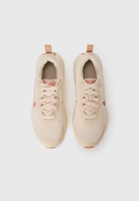 Ein Paar beiger Nike-Laufschuhe mit hellbraunen Akzenten, aus Netzstoff und Schnürsenkeln, von oben auf weißem Hintergrund gezeigt.