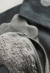 Grå lynlås taske med fluffy tekstur og glat stof. Indeholder et dekorativt element der ligner en blomst. Syet detaljering synlig.