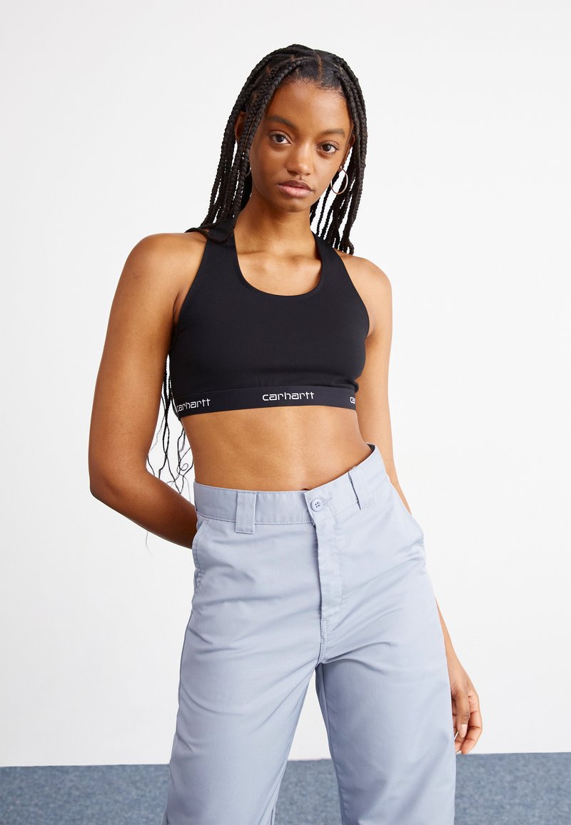 Black sports bra with a racerback design, featuring a branded elastic band. Paired with light gray, high-waisted pants. Smooth fabric texture.