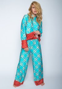Türkisfarbenes Pyjama-Set mit geometrischem Muster und roten Akzenten an den Bündchen und dem Taillenbund, aus glattem Stoff gefertigt. Lange Ärmel und Hosen.