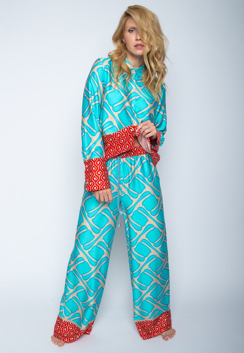 Türkisfarbenes Pyjama-Set mit geometrischem Muster und roten Akzenten an den Bündchen und dem Taillenbund, aus glattem Stoff gefertigt. Lange Ärmel und Hosen.