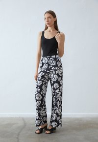 Débardeur noir associé à un pantalon large taille haute avec un motif floral noir et blanc. Tissu lisse avec un ajustement décontracté.