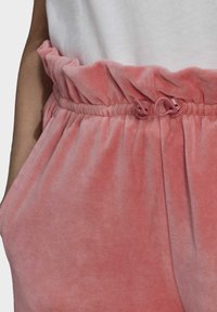 Pink, soft velvet pants feature a gathered waistband with pink drawstring toggles and side pockets, highlighting a comfortable, casual design.