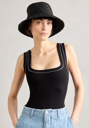 Svart ribbet bodysuit med firkantet utringning og sølvfarget søm, kombinert med høytlivede lyseblå denimshorts og en teksturert svart hatt.
