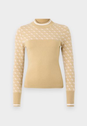 Beige neulepusero, jossa on valkoinen timanttimainen kuvio ylähihoissa, ribbaus kauluksessa ja hihoissa valkoisilla yksityiskohdilla.