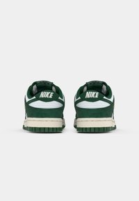 Baskets Nike en daim vert et en cuir blanc. Elles présentent une languette texturée, un col rembourré et une semelle en caoutchouc avec un motif de traction vert.