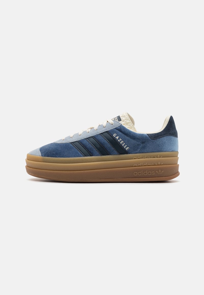 Modré tenisky Adidas Gazelle s vrstvou hnědé gumové podrážky a bílými tkaničkami, vystavené na bílém pozadí a směřující doprava.