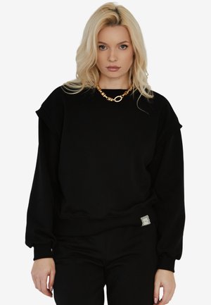 Czarny sweatshirt o luźnym kroju, z prążkowanymi mankietami i pasem, z teksturowaną metką po boku oraz okrągłym dekoltem.