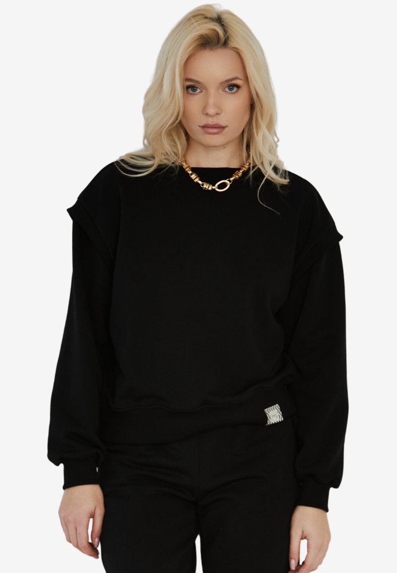 Czarny sweatshirt o luźnym kroju, z prążkowanymi mankietami i pasem, z teksturowaną metką po boku oraz okrągłym dekoltem.