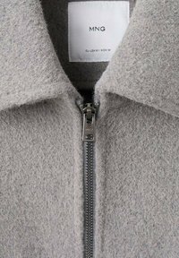 Giacca in misto lana grigia con colletto, zip frontale completa e etichetta in tessuto con dettagli del marchio. Texture morbida e linee pulite.