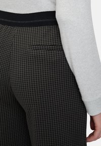 Schwarz-weiße Hahnentritt-Musterhose mit glatter Textur, ausgestattet mit einem schwarzen elastischen Bund und einem Rückentaschen-Detail.