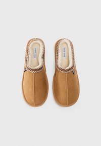 Une paire de chaussons en suède marron avec doublure en fausse fourrure blanche et couture en zigzag autour de l'ouverture, de la marque Pier One.