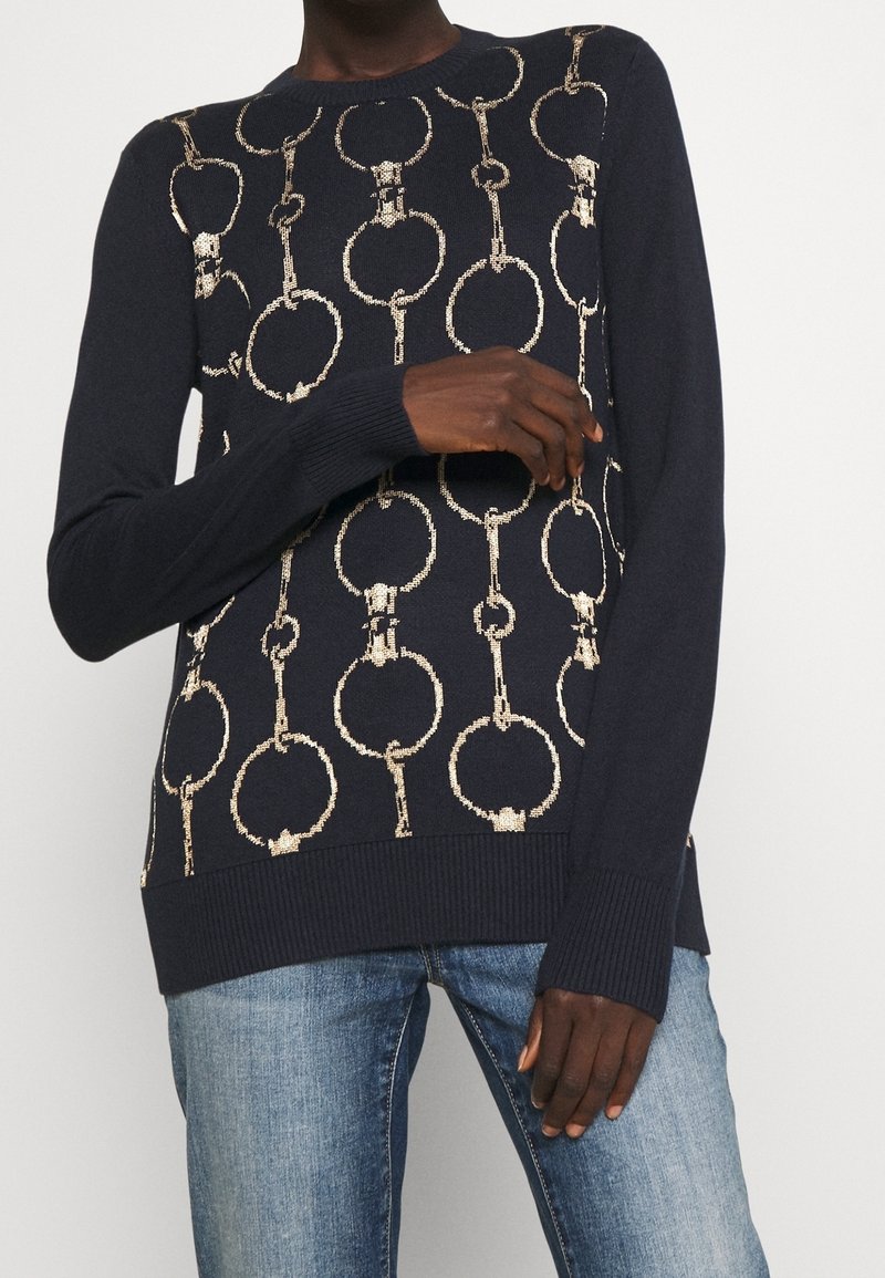 Tmavě modrý svetr s motivem zlatých řetězových oček. Vyrobený z měkké látky, má kulatý výstřih a žebrované manžety a lem.
