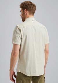 Beige Kurzarmhemd aus leichtem Stoff mit Button-down-Kragen und einem Aufnäher auf der linken Schulter.