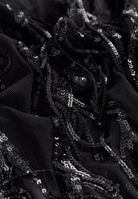 Tissu en maille noire orné de sequins noirs superposés, présentant une apparence texturée et en couches avec des accents brillants sur toute la surface.